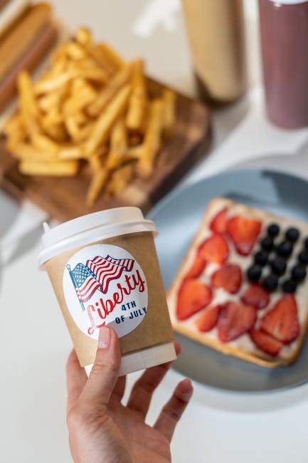 Hand holding a coffee cup with 'Liberty 4th of July' sticker near themed toast